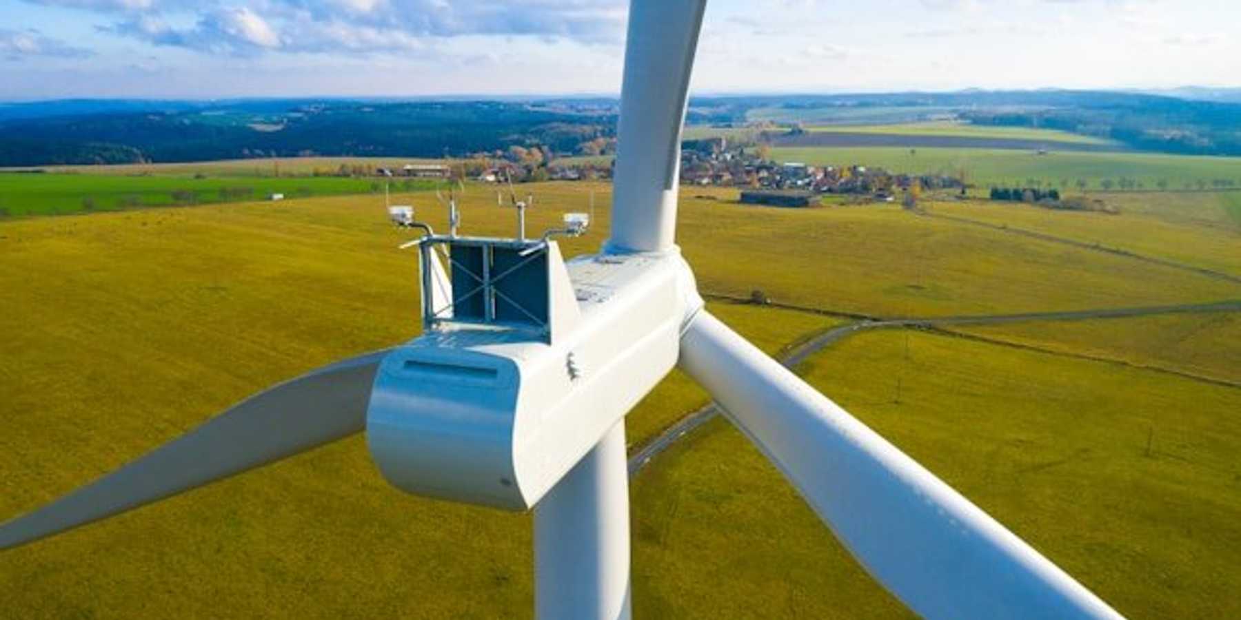 A closeup of a wind turbine with green fields in the background.