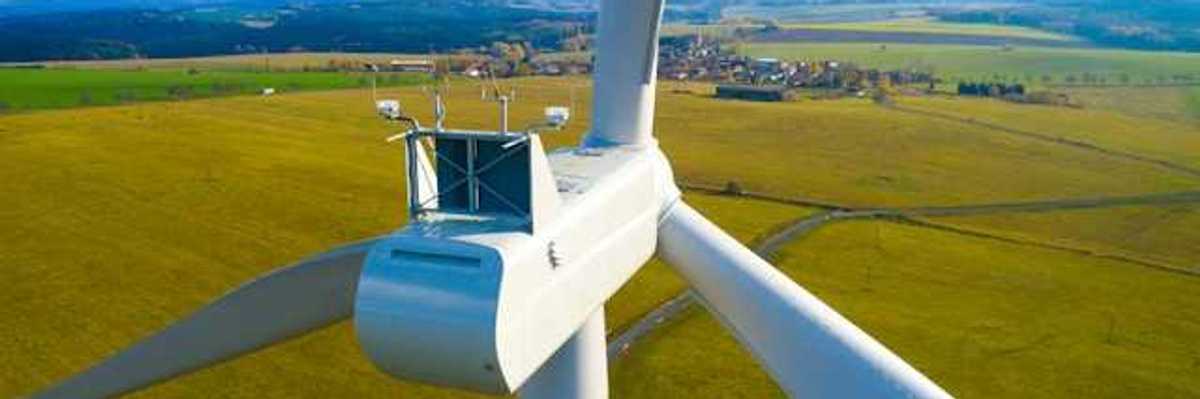 A closeup of the top of a wind turbine with farm fields in the background