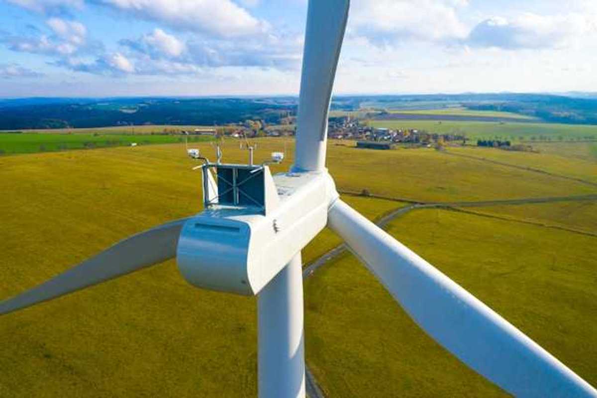 A closeup of the top of a wind turbine with farm fields in the background