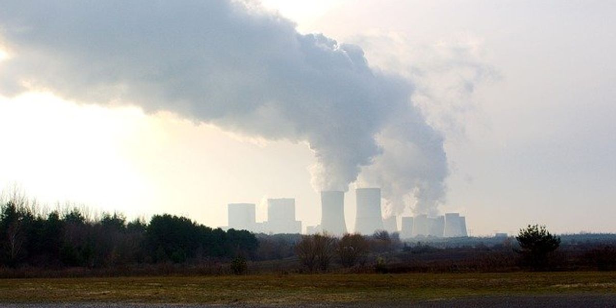A coal power plant in the distance with smoke billowing from the towers.