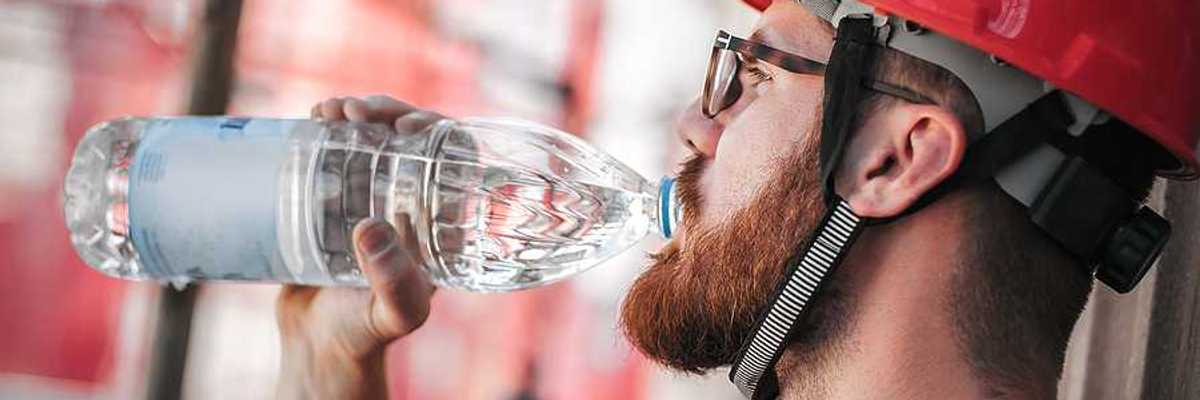 A construction worker in a red hard hat drinking from a plastic water bottle