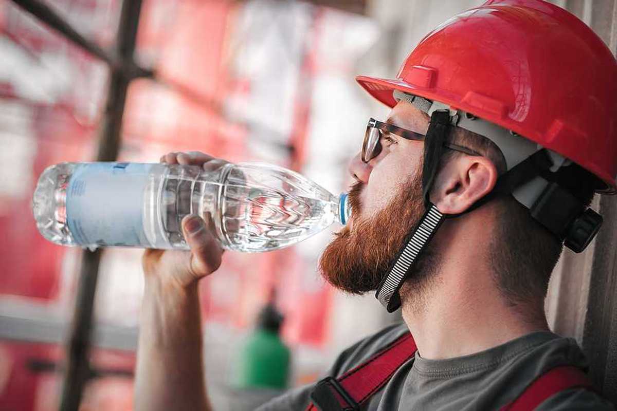 A construction worker in a red hard hat drinking from a plastic water bottle