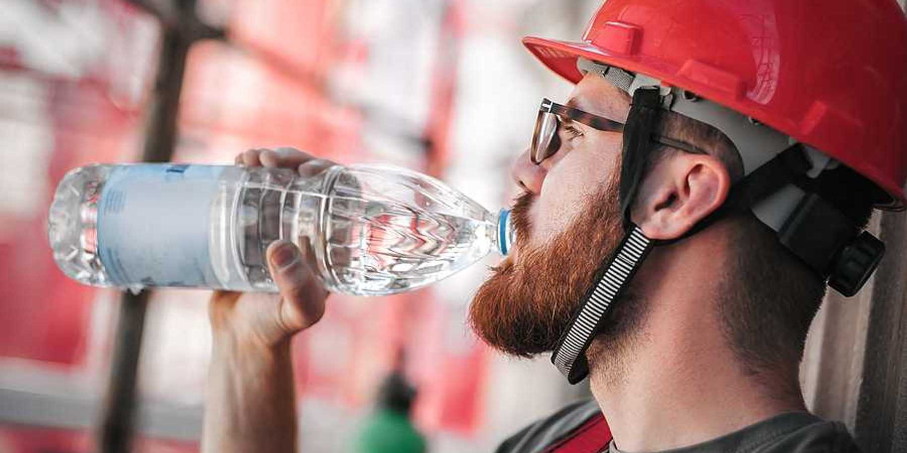 A construction worker in a red hard hat drinking from a plastic water bottle