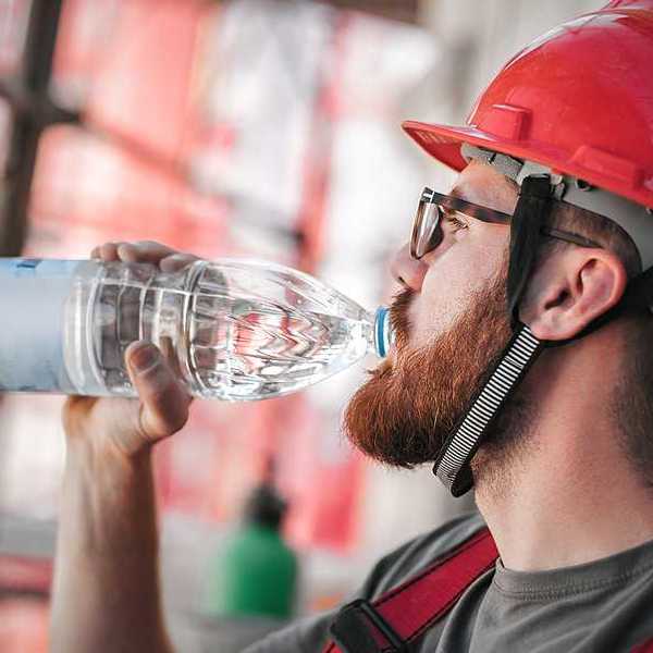 A construction worker in a red hard hat drinking from a plastic water bottle