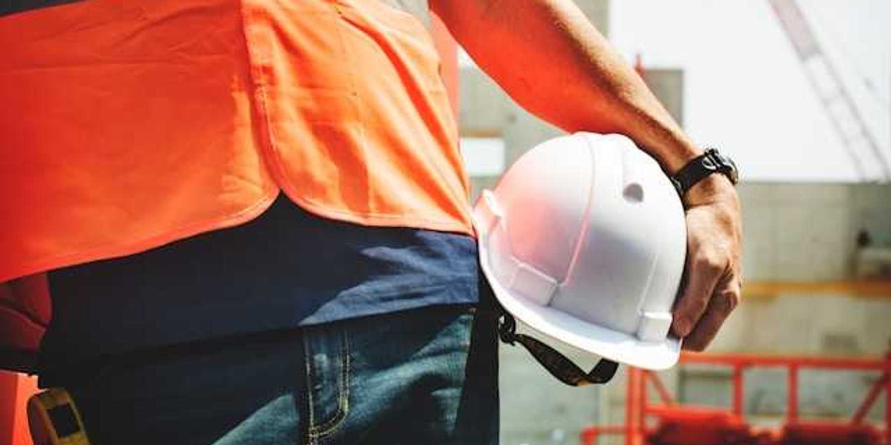 A construction worker in an orange vest carrying a white hard hat on a sunny day