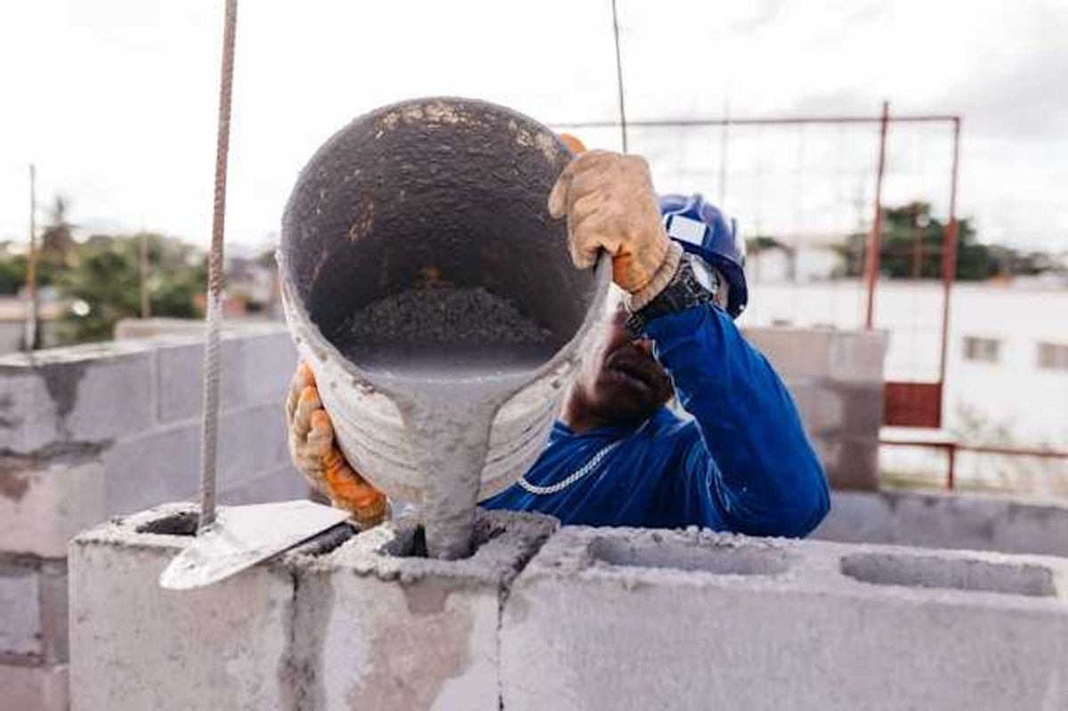 A construction worker pouring cement into open bricks
