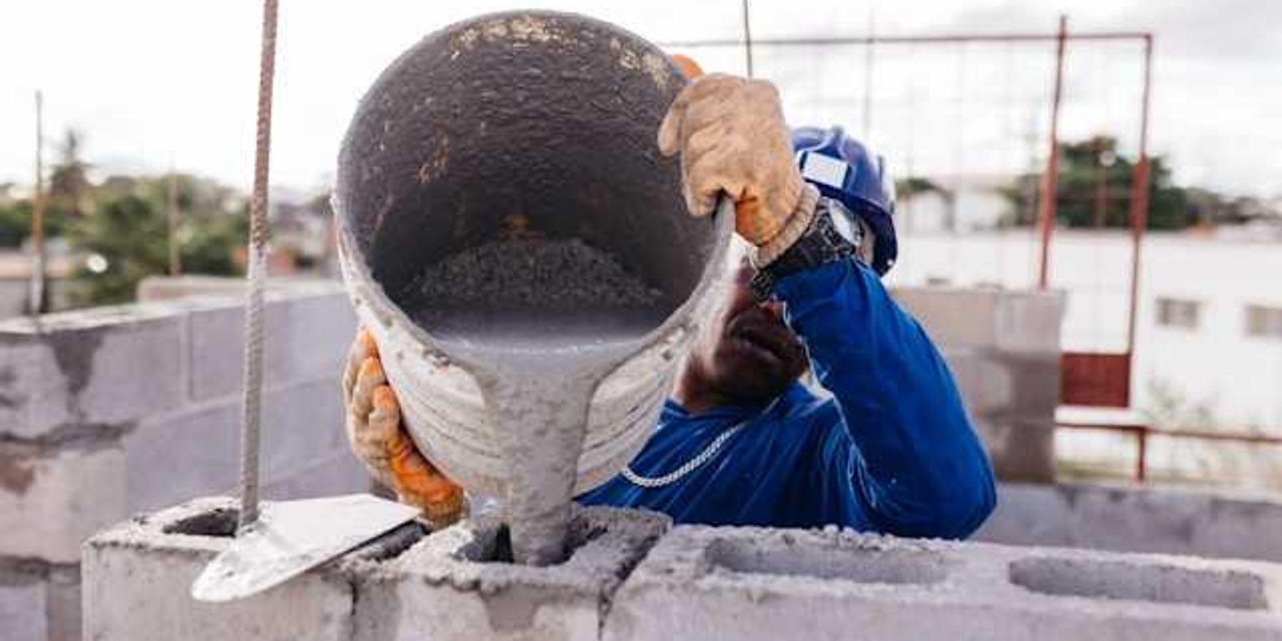 A construction worker pouring cement into open bricks