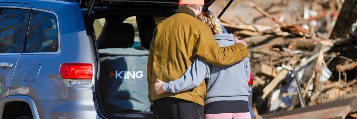 a couple of people standing next to a car in front of a destroyed home