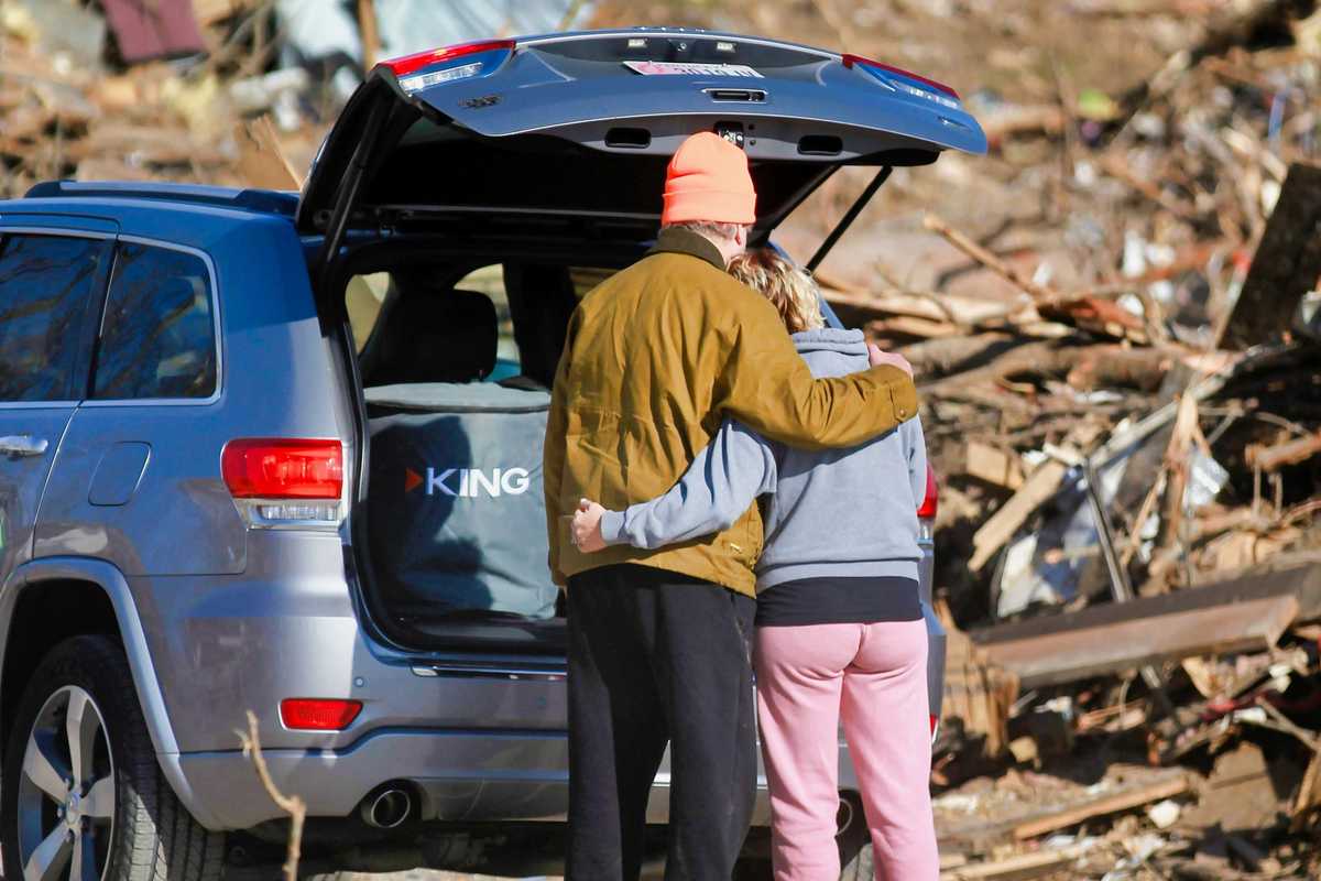 a couple of people standing next to a car in front of a destroyed home