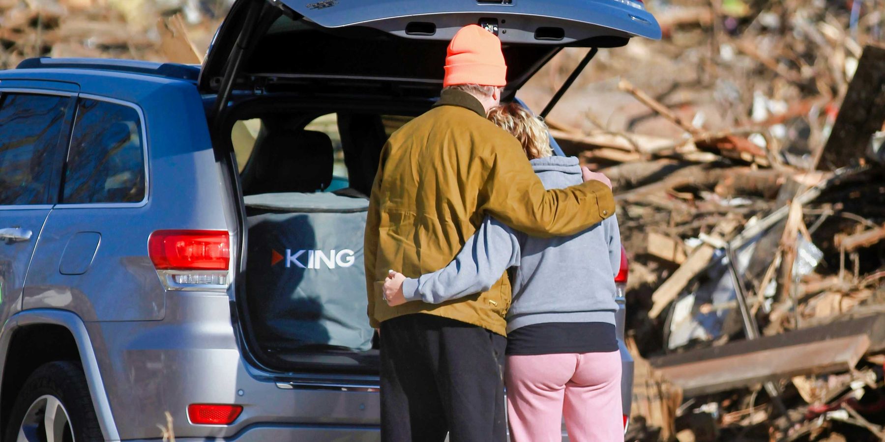 a couple of people standing next to a car in front of a destroyed home