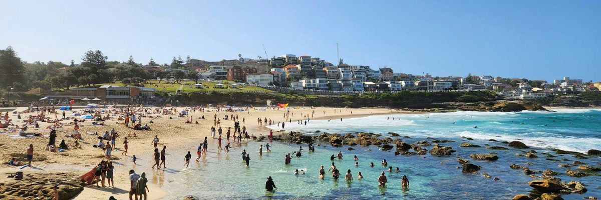 a crowded beach with lots of people on it and buildings in background.