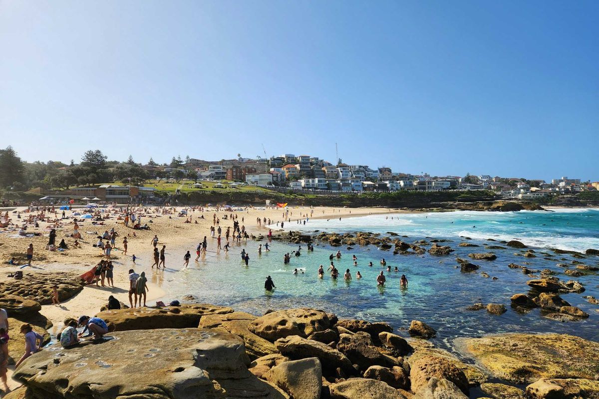a crowded beach with lots of people on it and buildings in background.