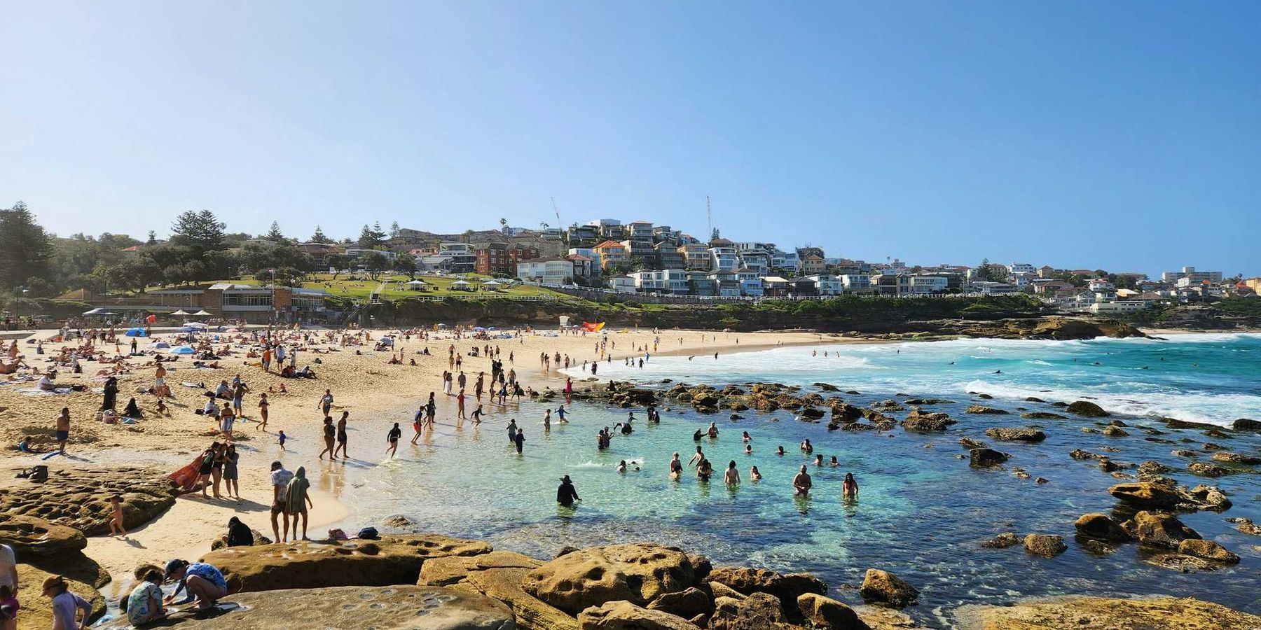 a crowded beach with lots of people on it and buildings in background.