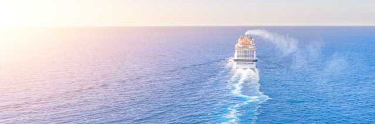 A cruise ship in the middle of the ocean with the sun setting to the left