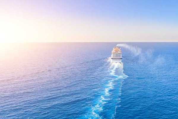 A cruise ship in the middle of the ocean with the sun setting to the left