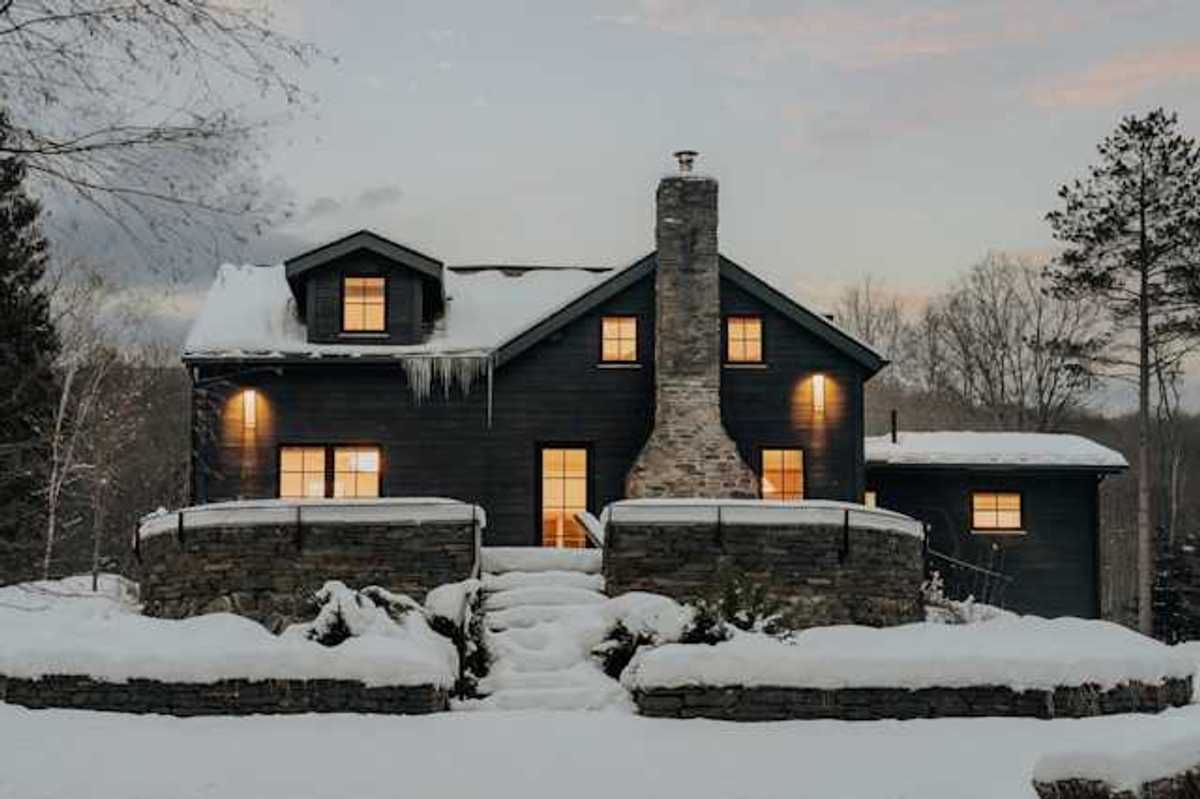 A dark house covered in snow with warm light coming from all of the windows