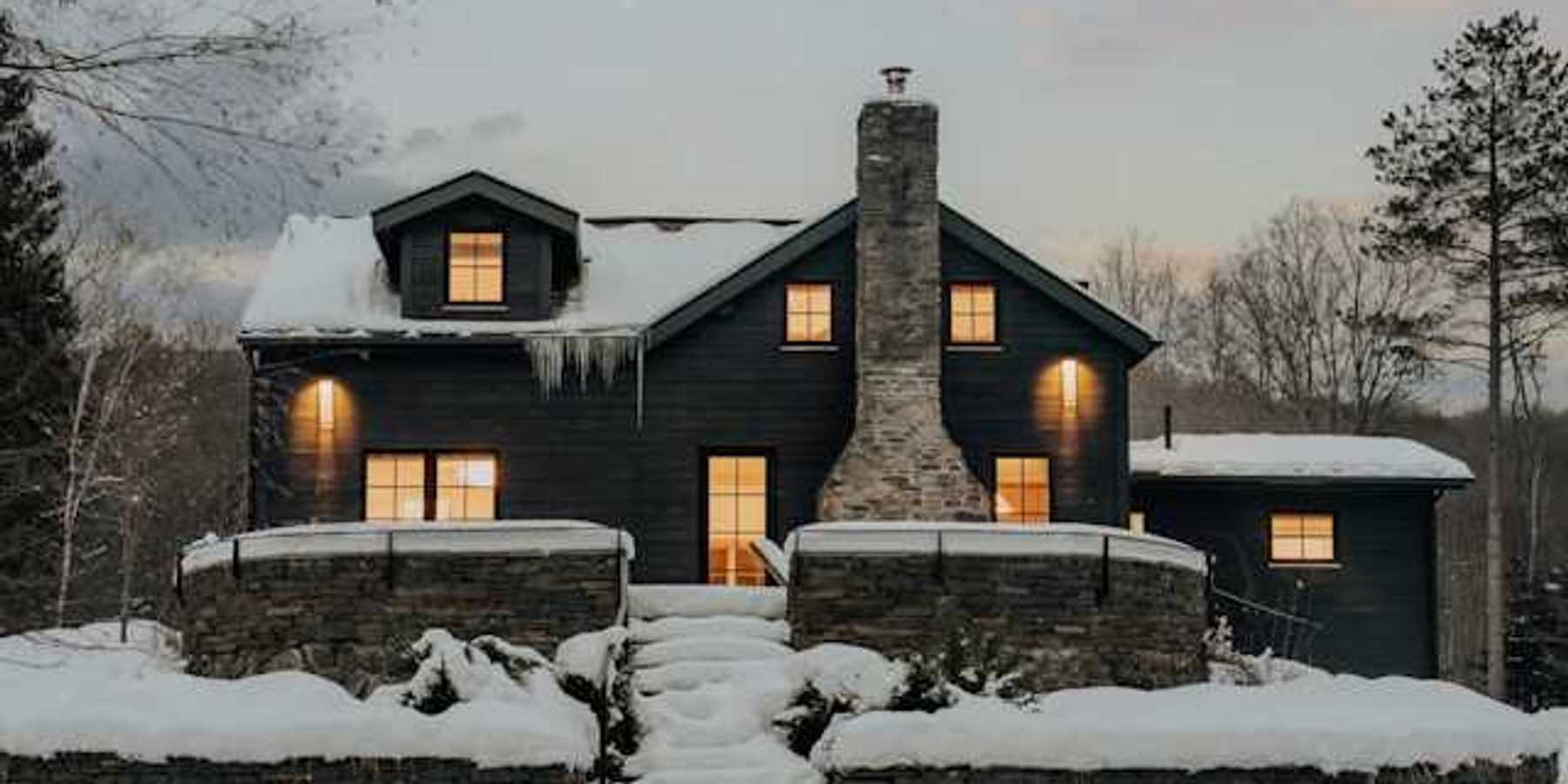 A dark house covered in snow with warm light coming from all of the windows