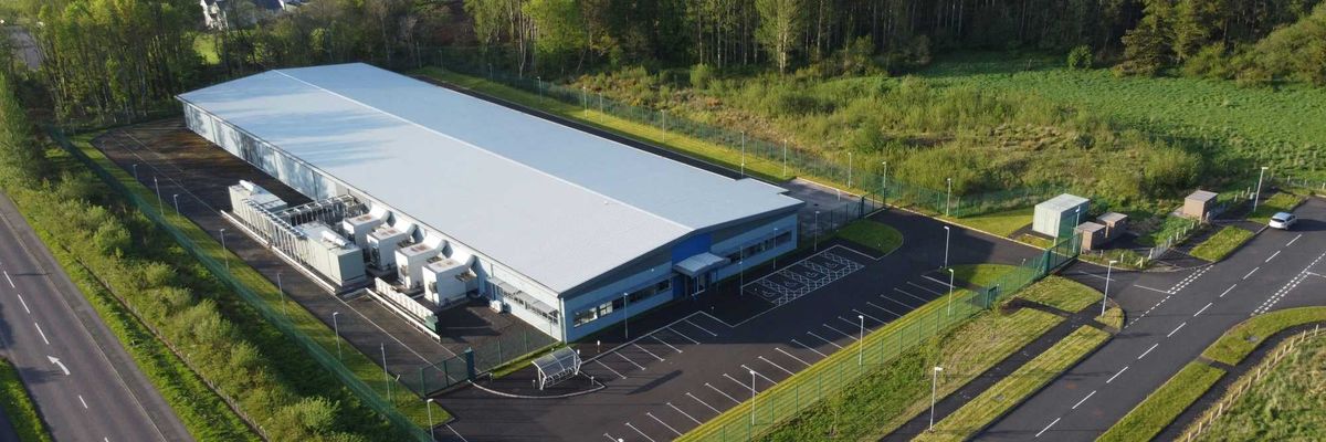 A data center situated in a green landscape and flanked by roads and trees.