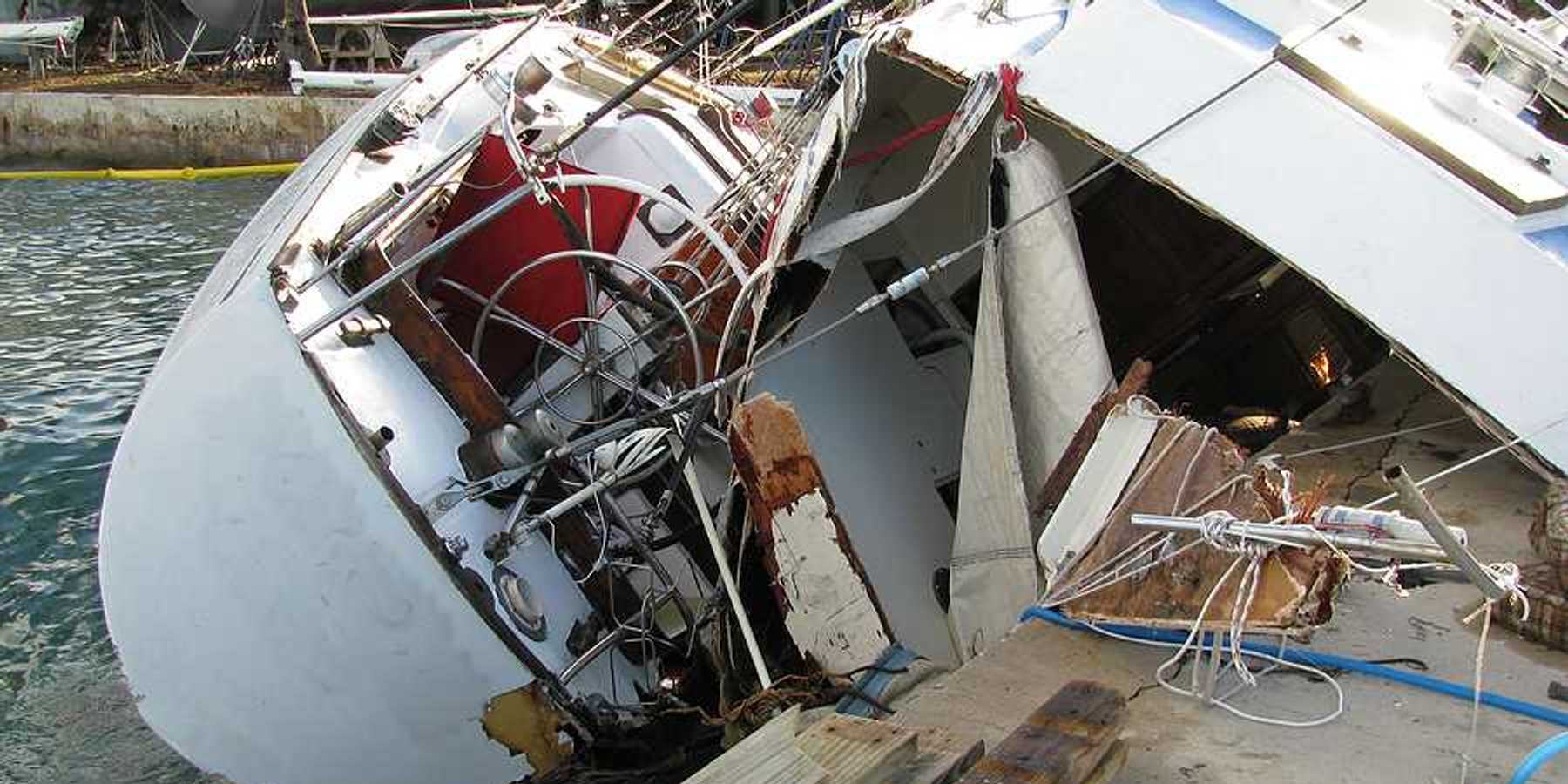 A destroyed boat leaning against a dock after a hurricane
