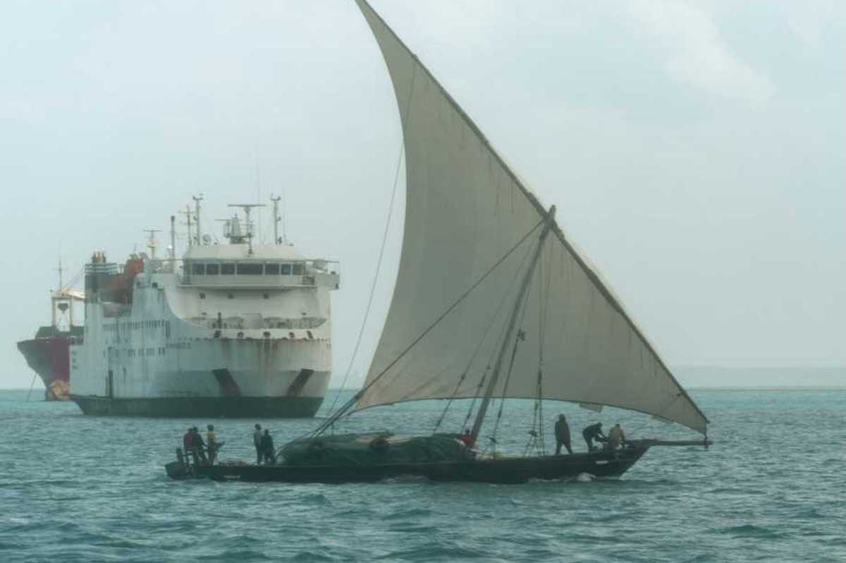 A dhow, a traditional sailing vessel for the region, sailing past a larger ship near the port of Zanzibar, Tanzania.