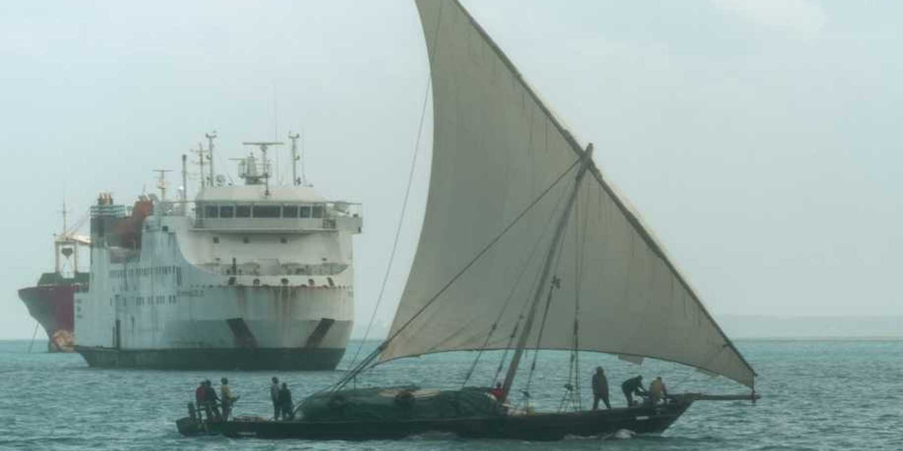 A dhow, a traditional sailing vessel for the region, sailing past a larger ship near the port of Zanzibar, Tanzania.