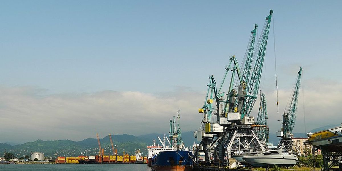 A dock with ships and cranes and mountains in the background.