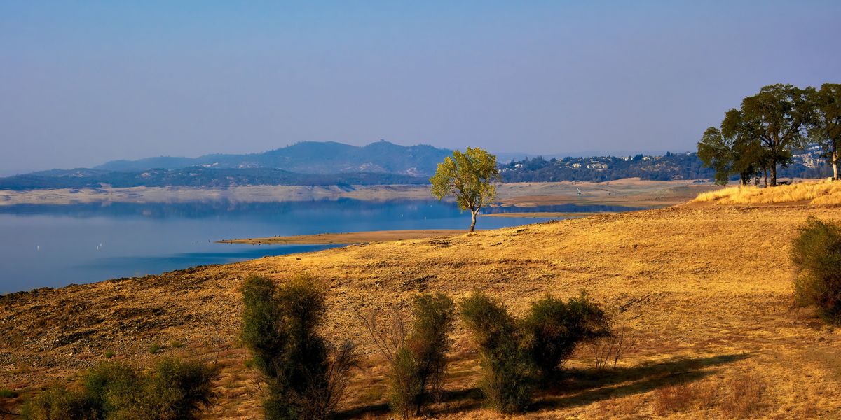 A dry field next to a reservoir with low water levels.
