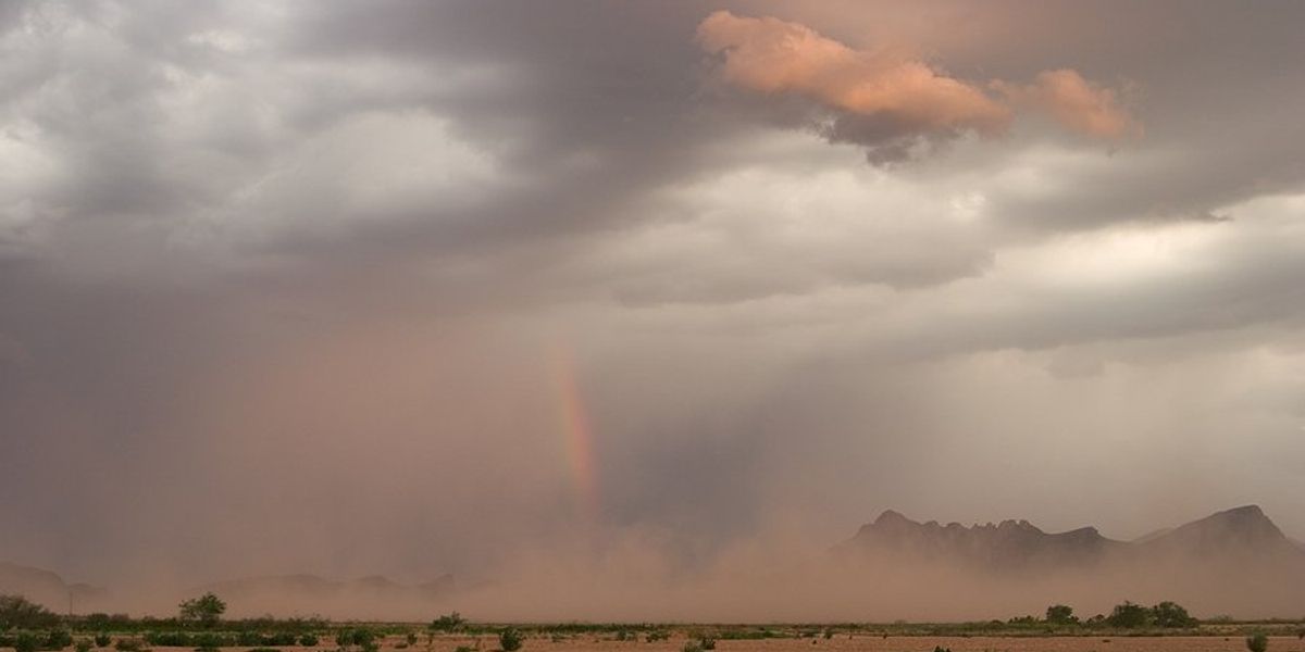 A dry landscape with a dust storm and a rainbow in the distance.