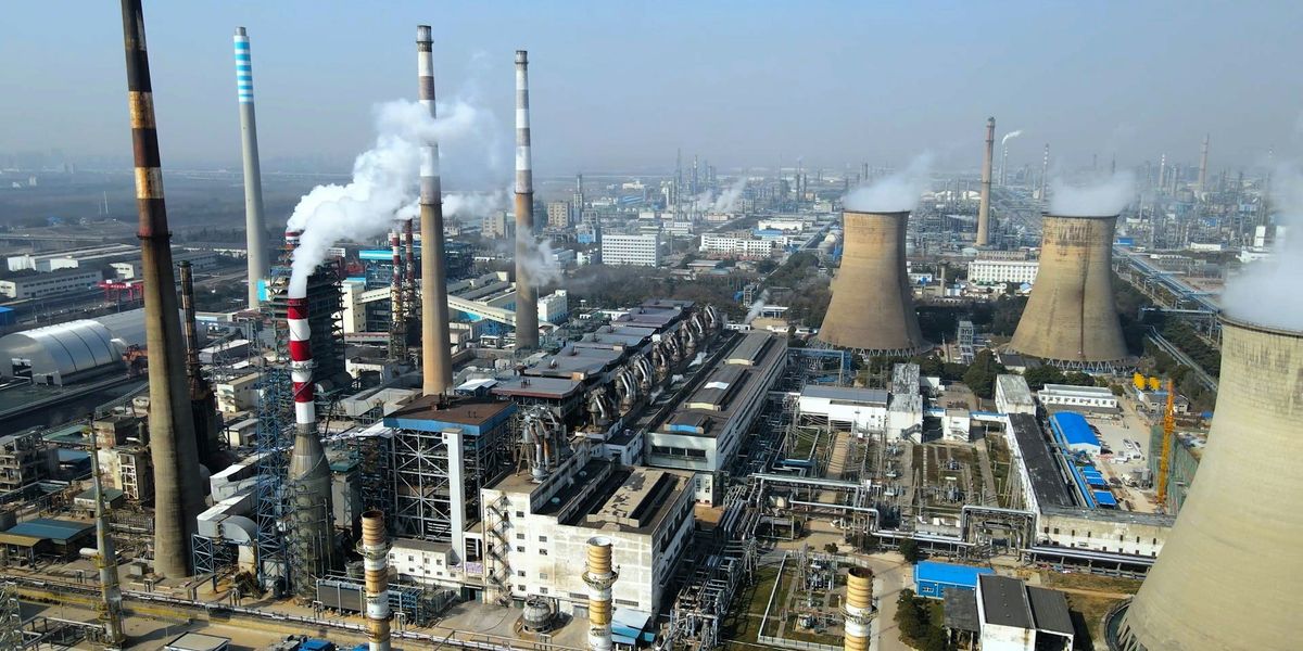 A factory complex emits pollutioni through several smokestacks with hazy skies in background.