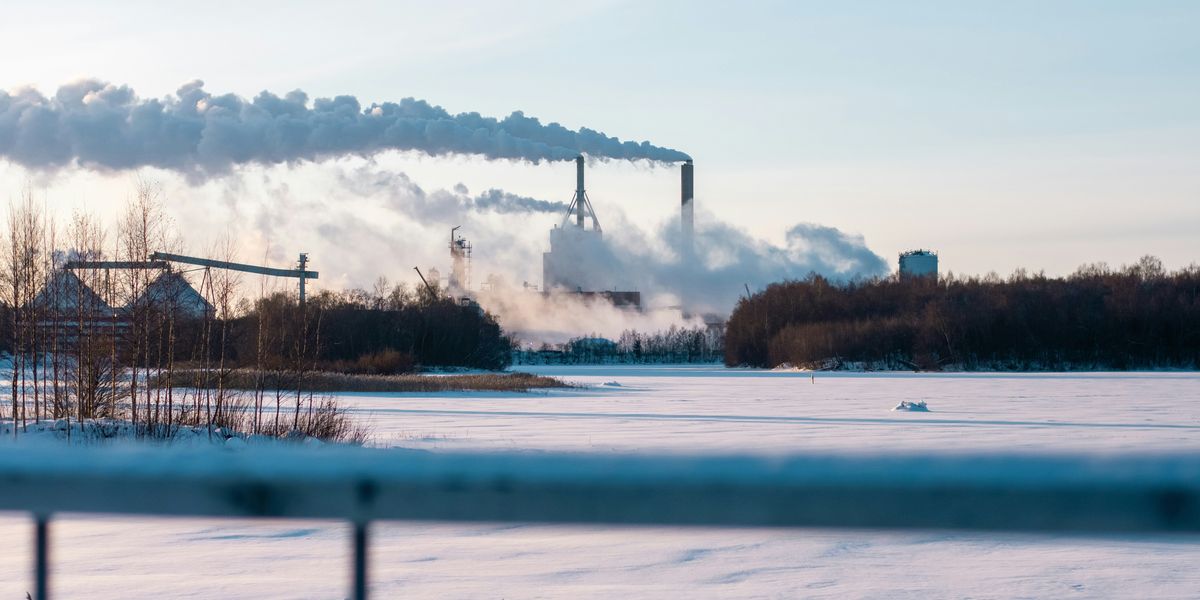 a factory with smoke pouring out of its stacks and a snow-covered foreground.