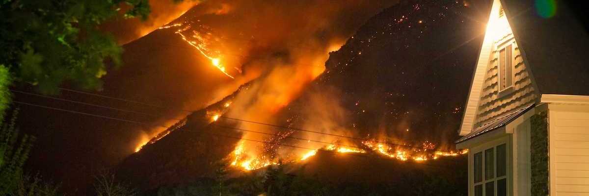 A family watches a nearby wildfire from their front lawn as flames cover a nearby mountainside in a nighttime setting