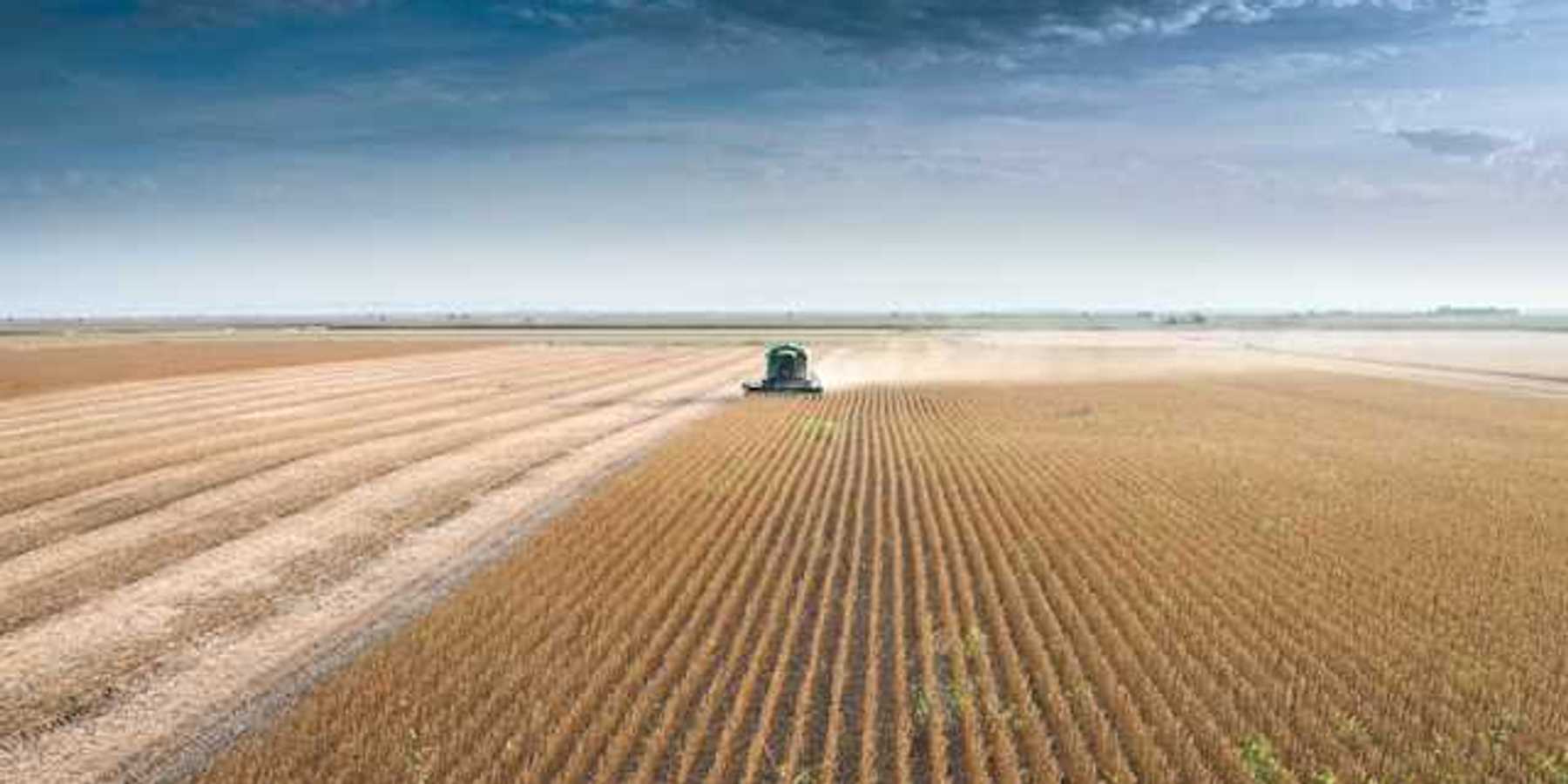 A farm tractor driving across a dry field