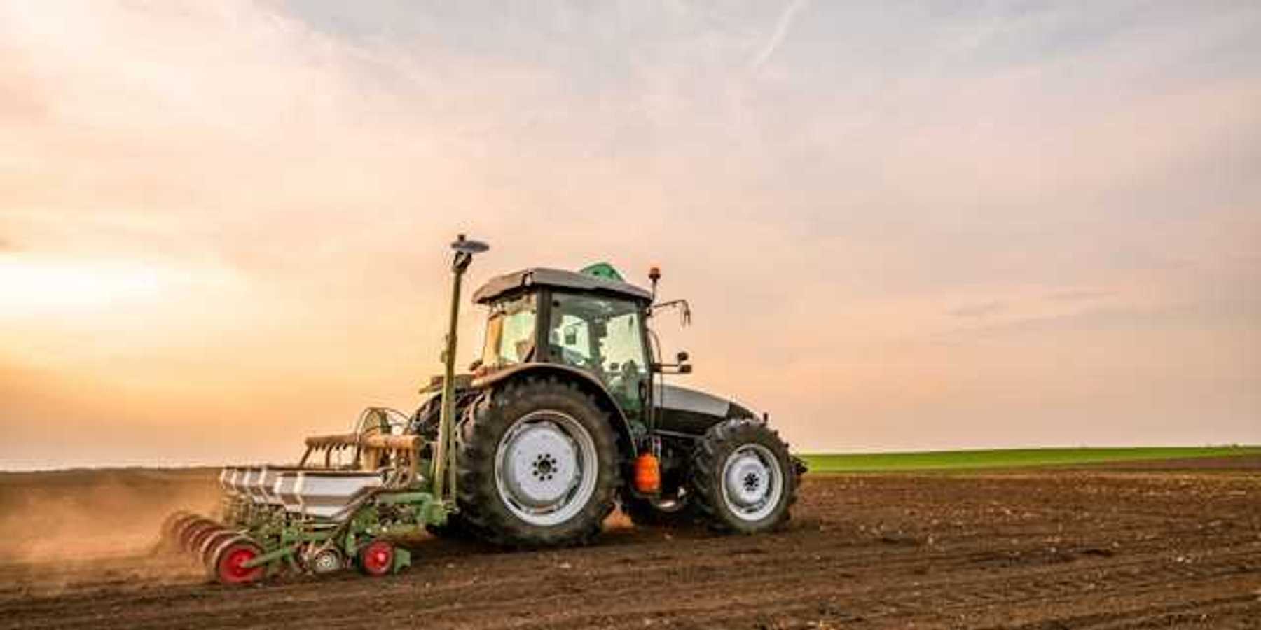 A farm tractor driving across a field of soil