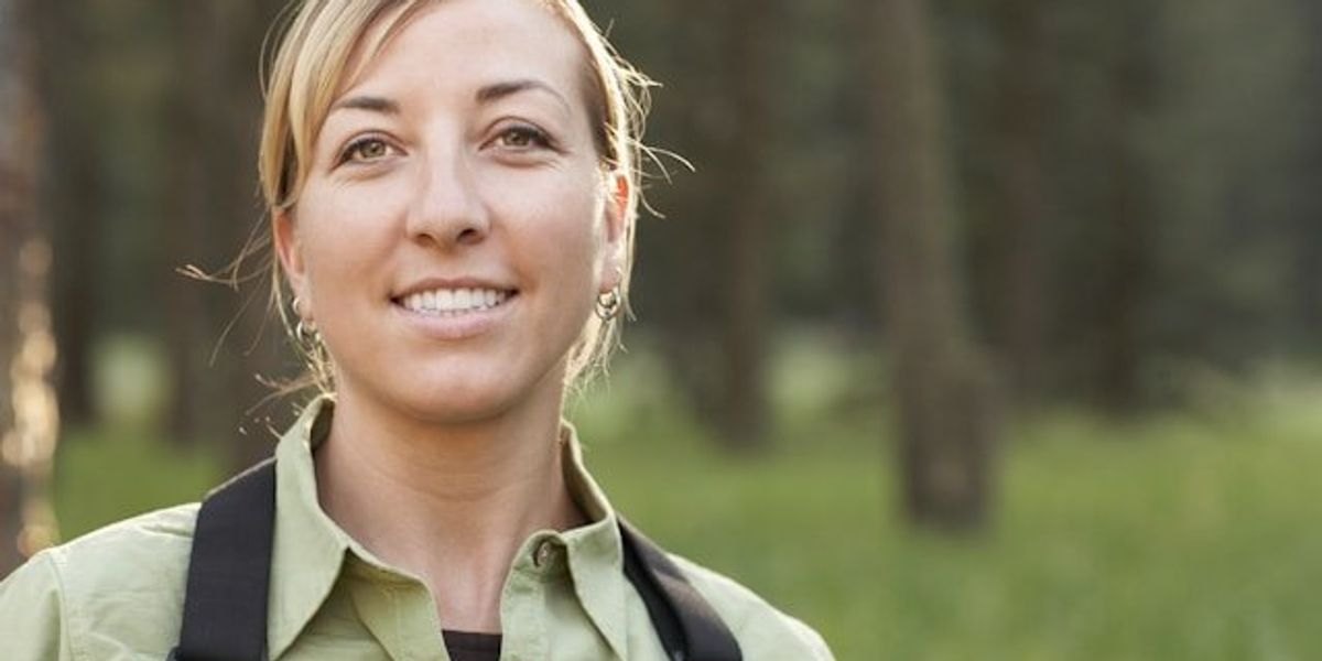 A female hiker in a green shirt with a black backpack looking into the camera.