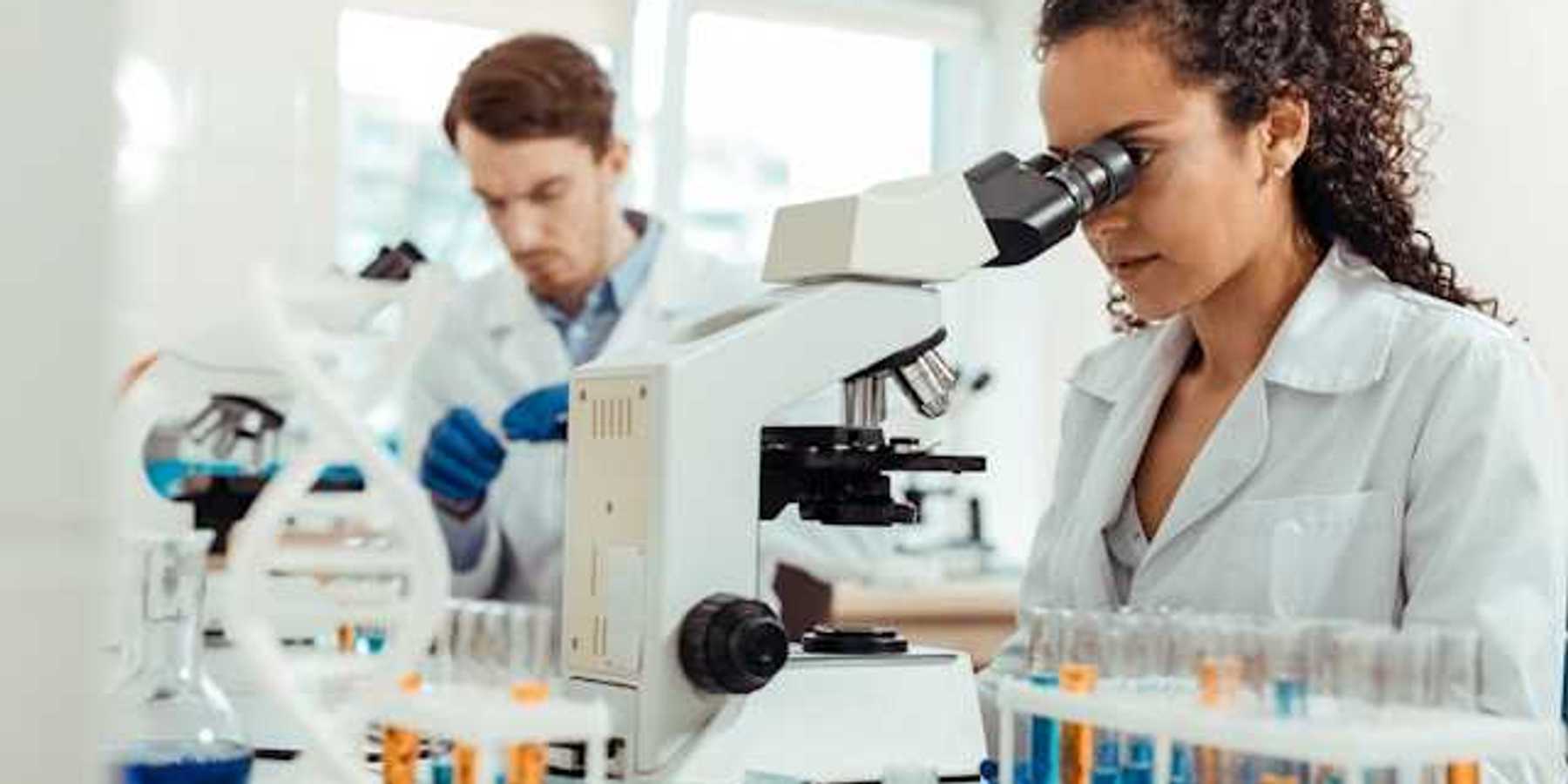 A female scientist standing at a lab table looking into a microscope