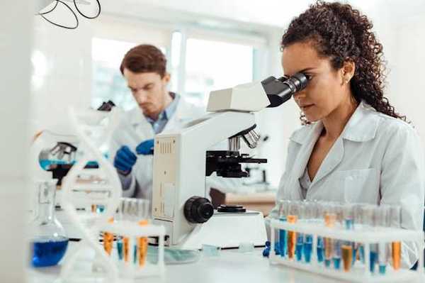 A female scientist standing at a lab table looking into a microscope