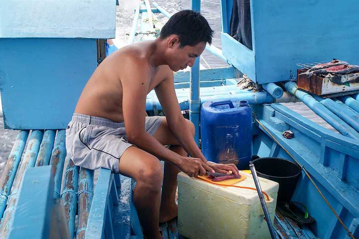 A filipino fisherman filleting a fish on his boat