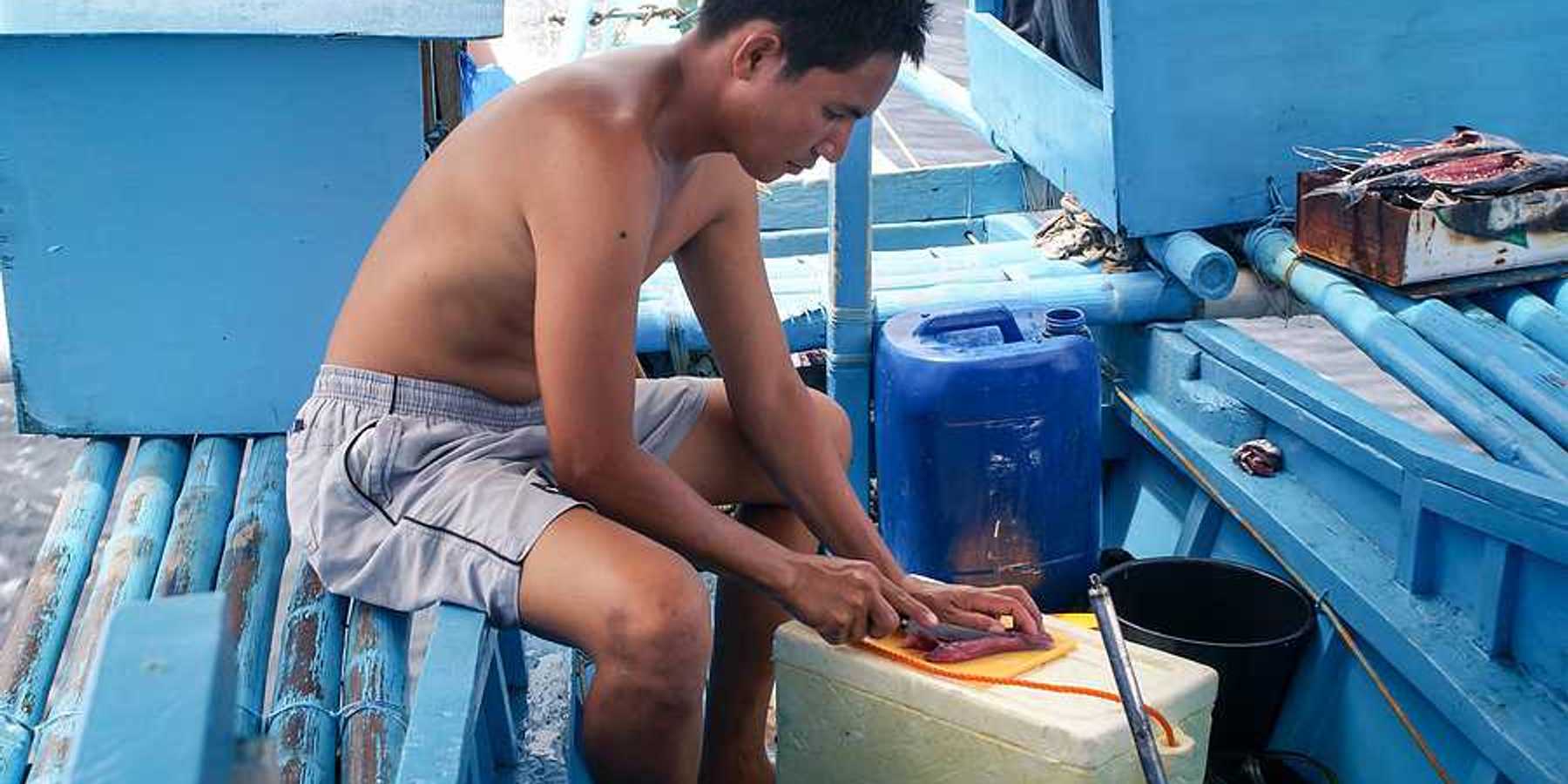 A filipino fisherman filleting a fish on his boat