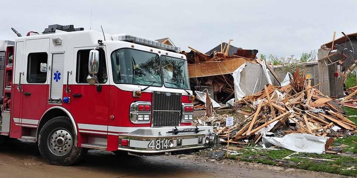 A firetruck parked in front of a home destroyed by a tornado