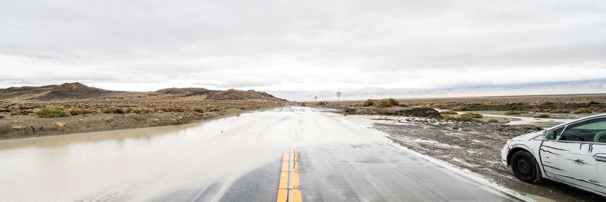 A flooded highway with a white car pulled over in the mud.