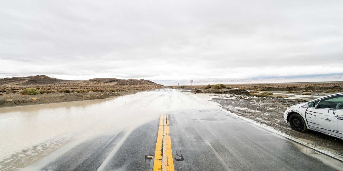 A flooded highway with a white car pulled over in the mud.