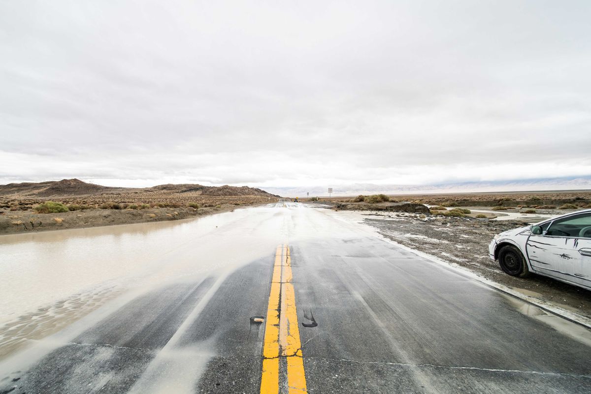 A flooded highway with a white car pulled over in the mud.