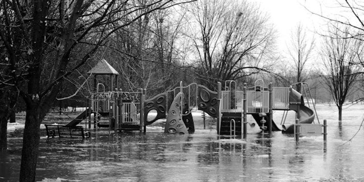 A flooded playground surrounded by bare trees, in black and white.