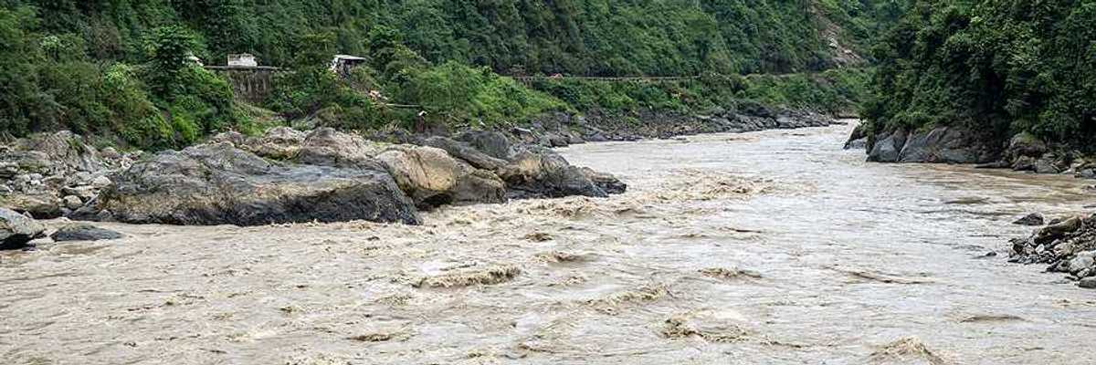A flooded river lined with rocks in a valley between two green hills