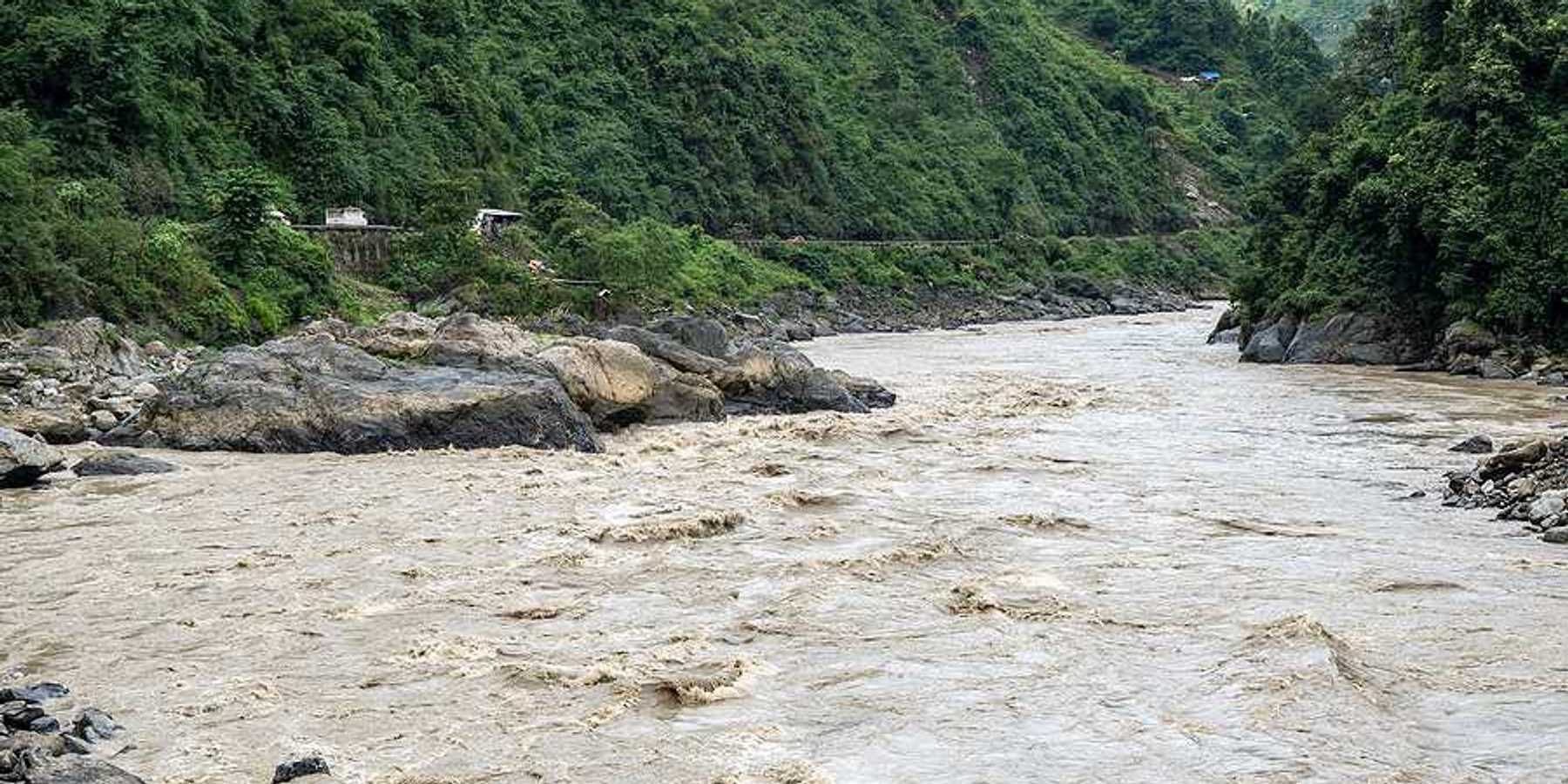A flooded river lined with rocks in a valley between two green hills