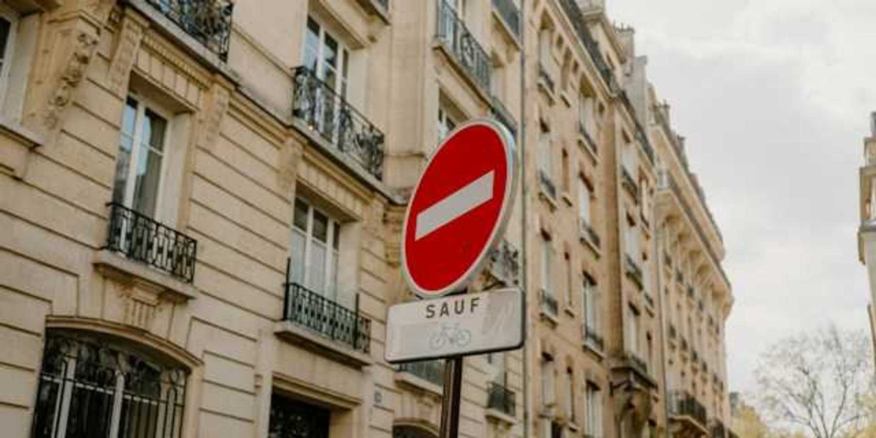 A French sign restricting cars from a street with Parisian buildings in the background