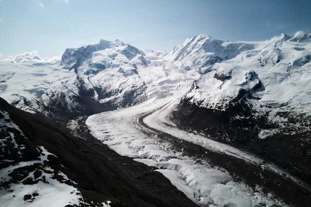 A glacier flowing down a valley under a snowy mountain range