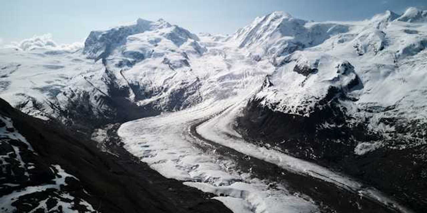 A glacier flowing down a valley under a snowy mountain range