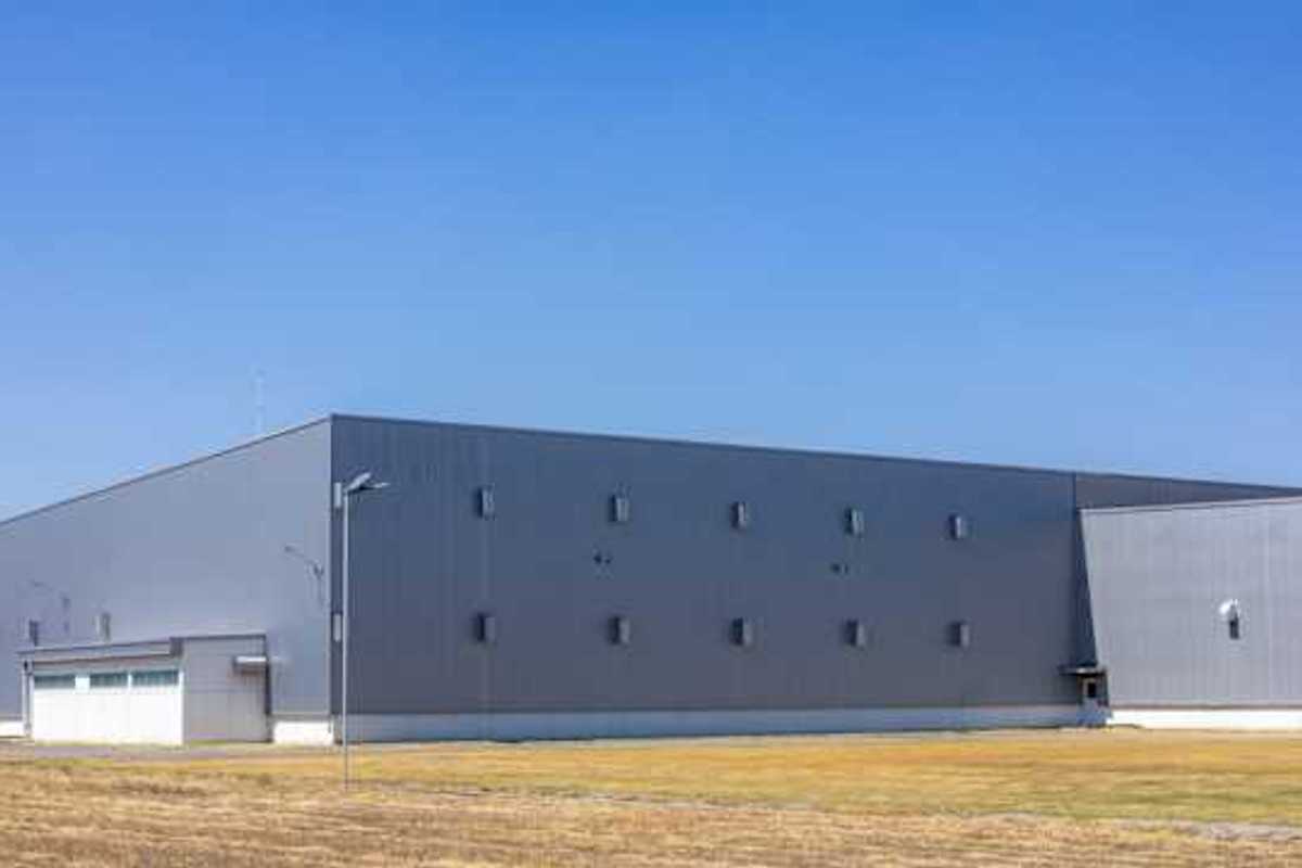 A gray warehouse type building on a brown field on a sunny day