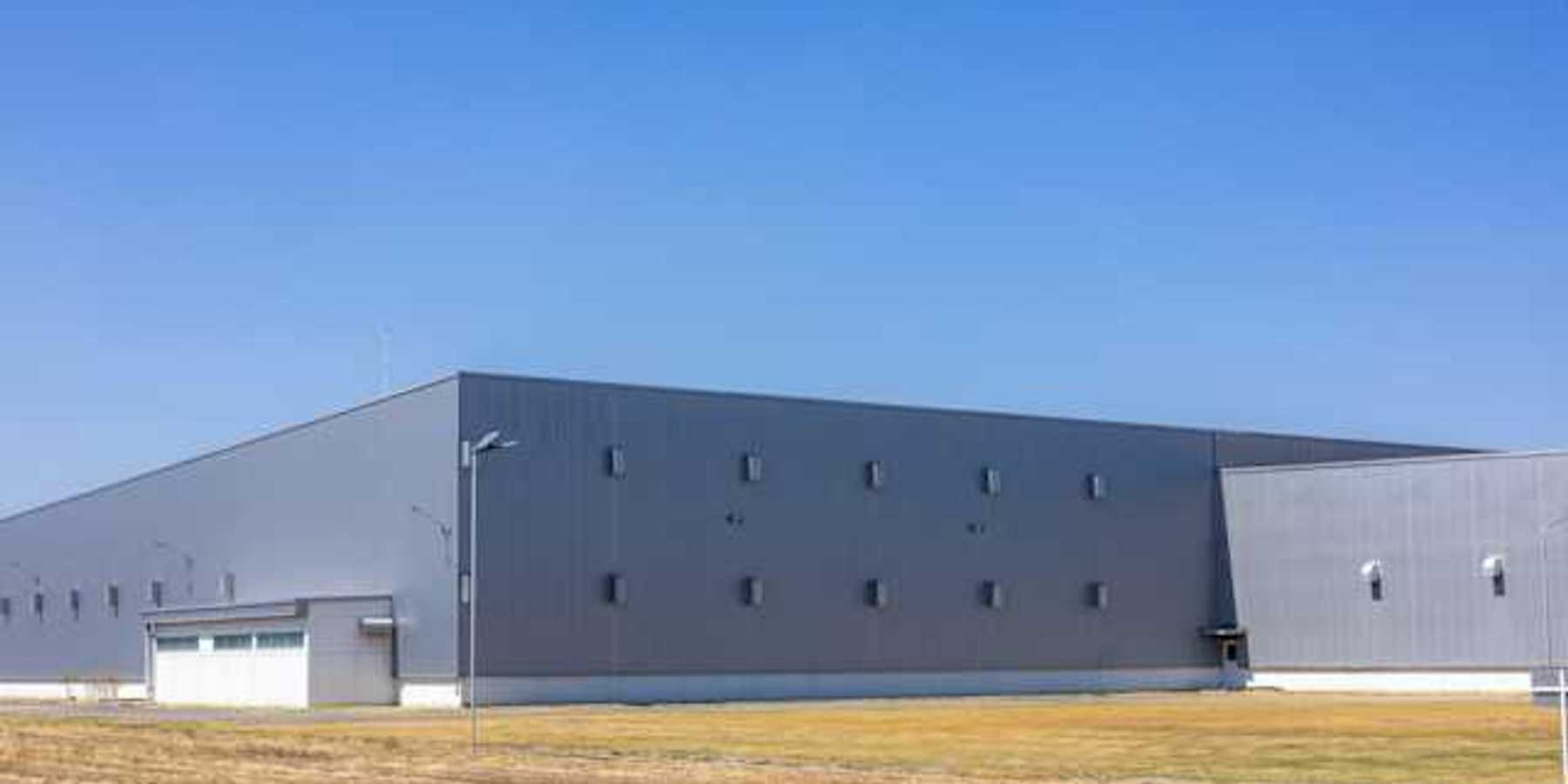 A gray warehouse type building on a brown field on a sunny day